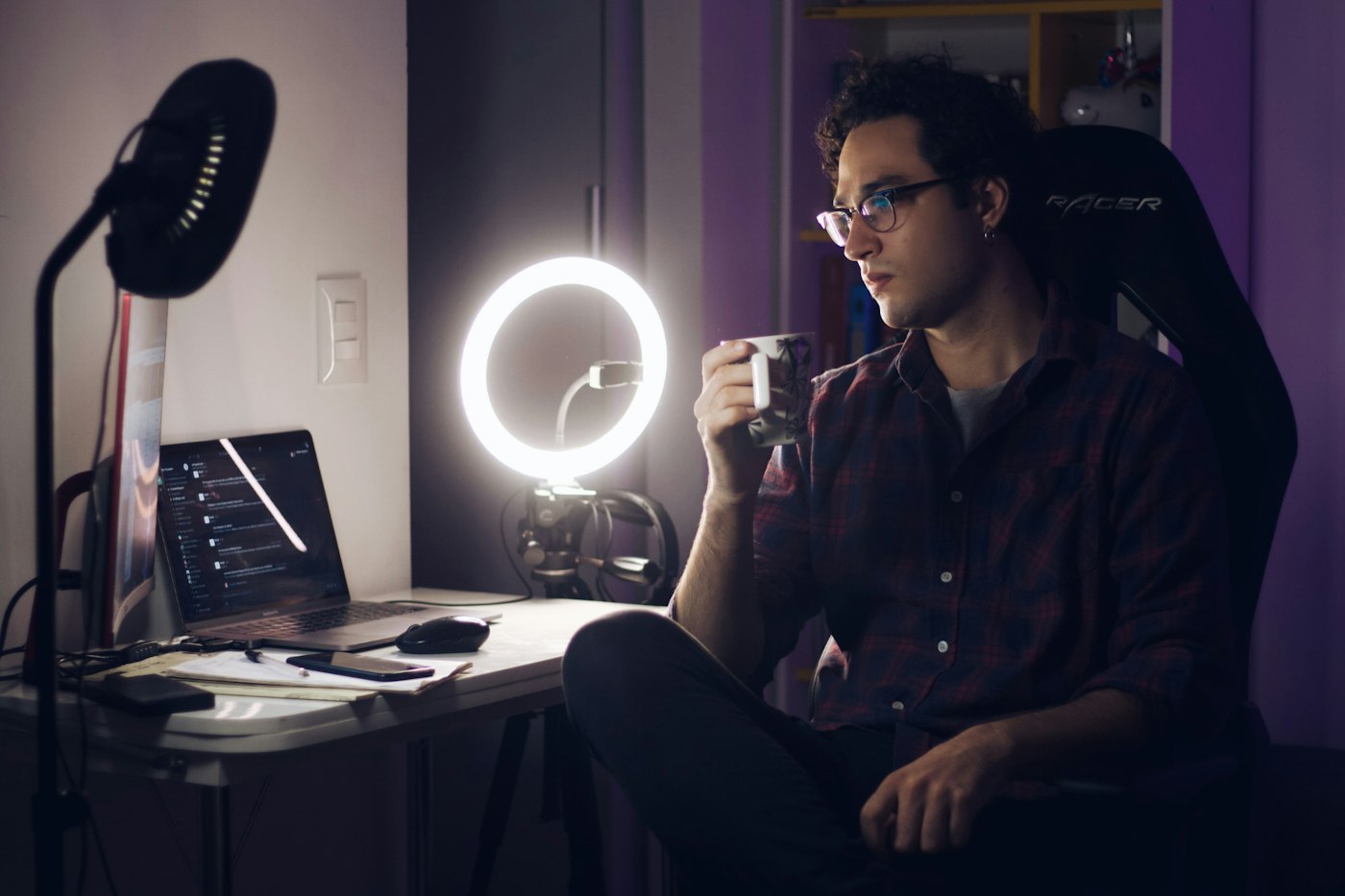 A creator at a ring-lit desk reviewing a stream on his laptop.