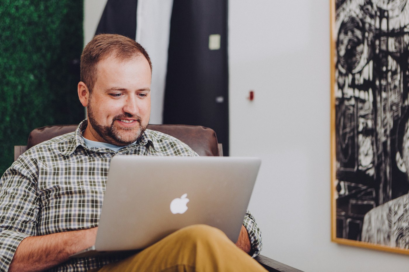 A freelancer smiling at his laptop in a bright room.