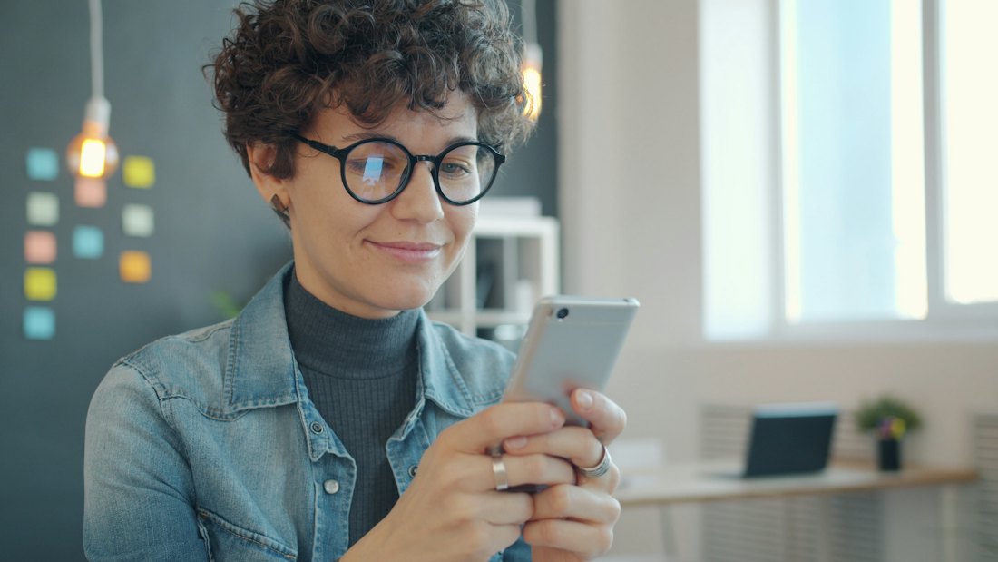 Someone smiling at their phone in a bright room.