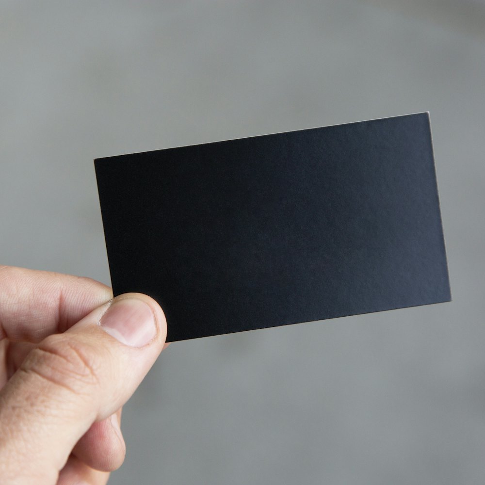 A matte black NFC smart business card held between two fingers